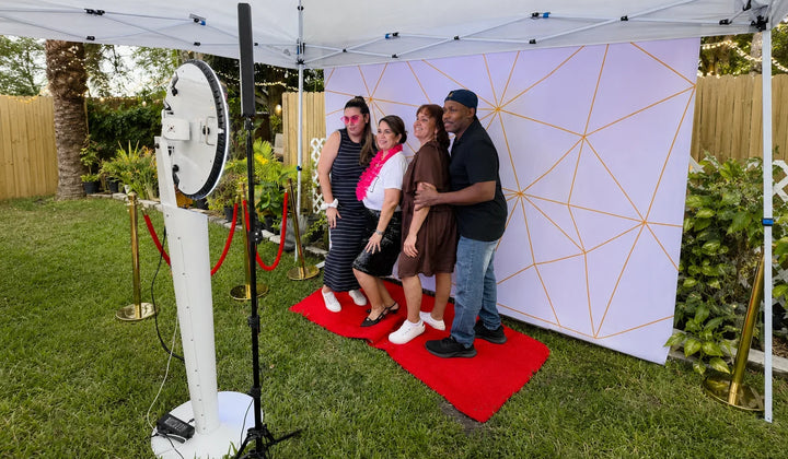Guests posing at an outdoor 360 photo booth setup under a canopy