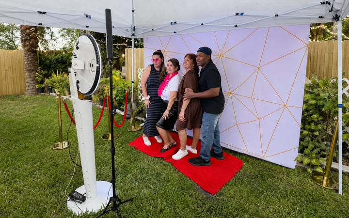 Guests posing at an outdoor 360 photo booth setup under a canopy