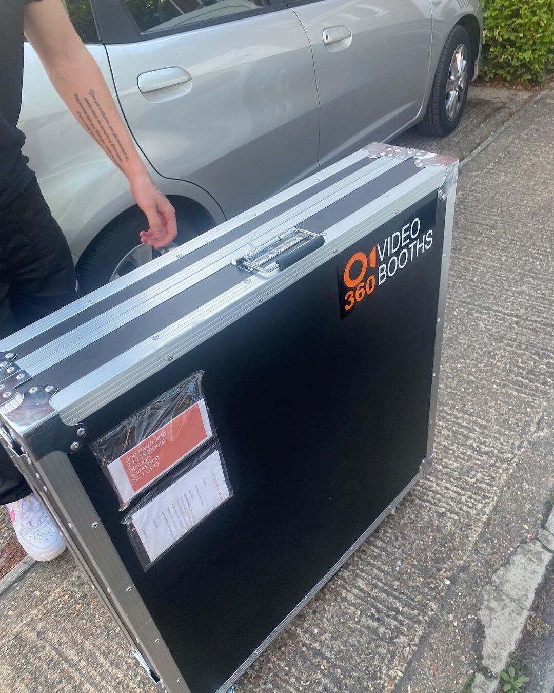 Person carrying the hard flight case for a Spin Metal 360 photo booth beside a car.