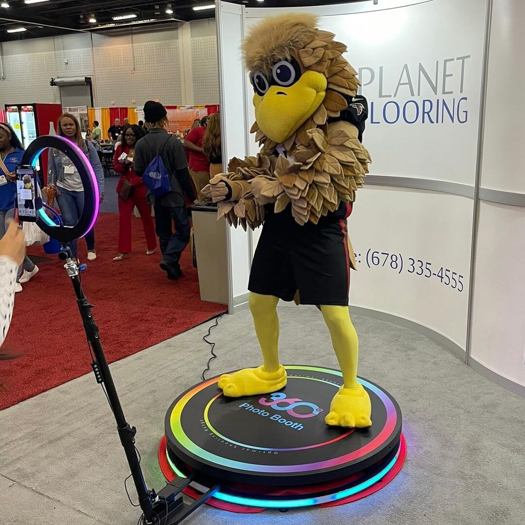 Spin Metal 360 photo booth with a mascot at a trade show.