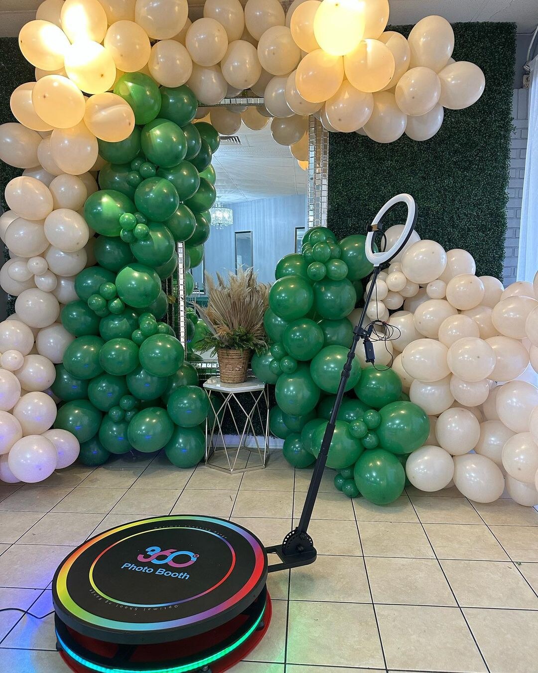 Spin Metal 360 photo booth in front of a green balloon backdrop.